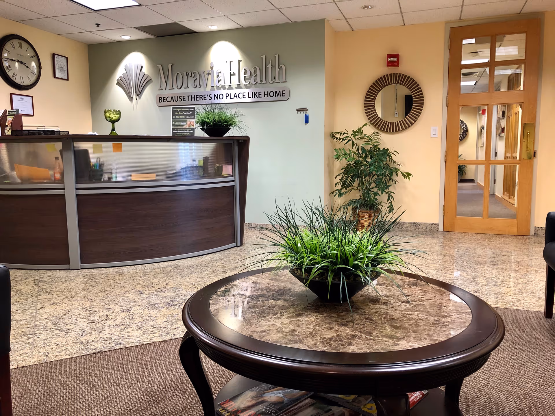 Moravia Health reception area with curved desk, greenery, and glass door.