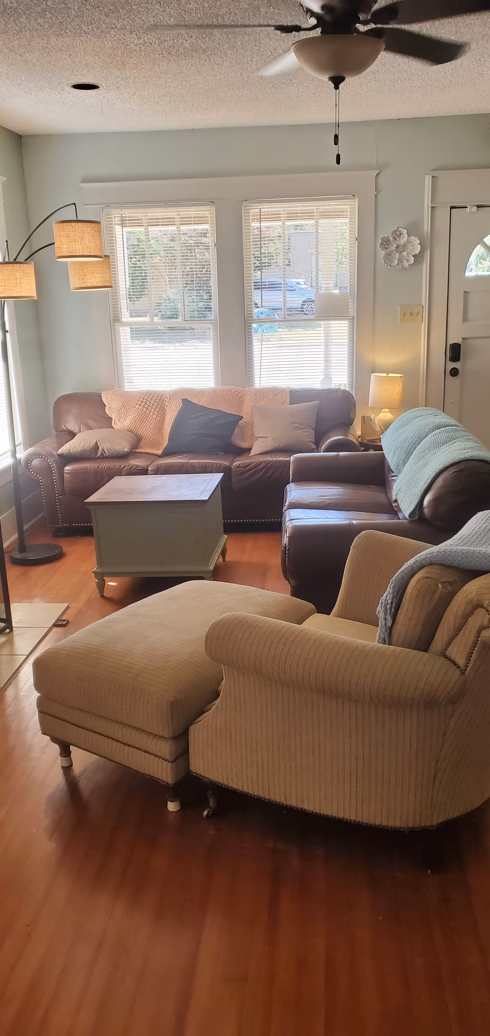 Cozy living room with leather couch, armchairs, a coffee table, and a ceiling fan.