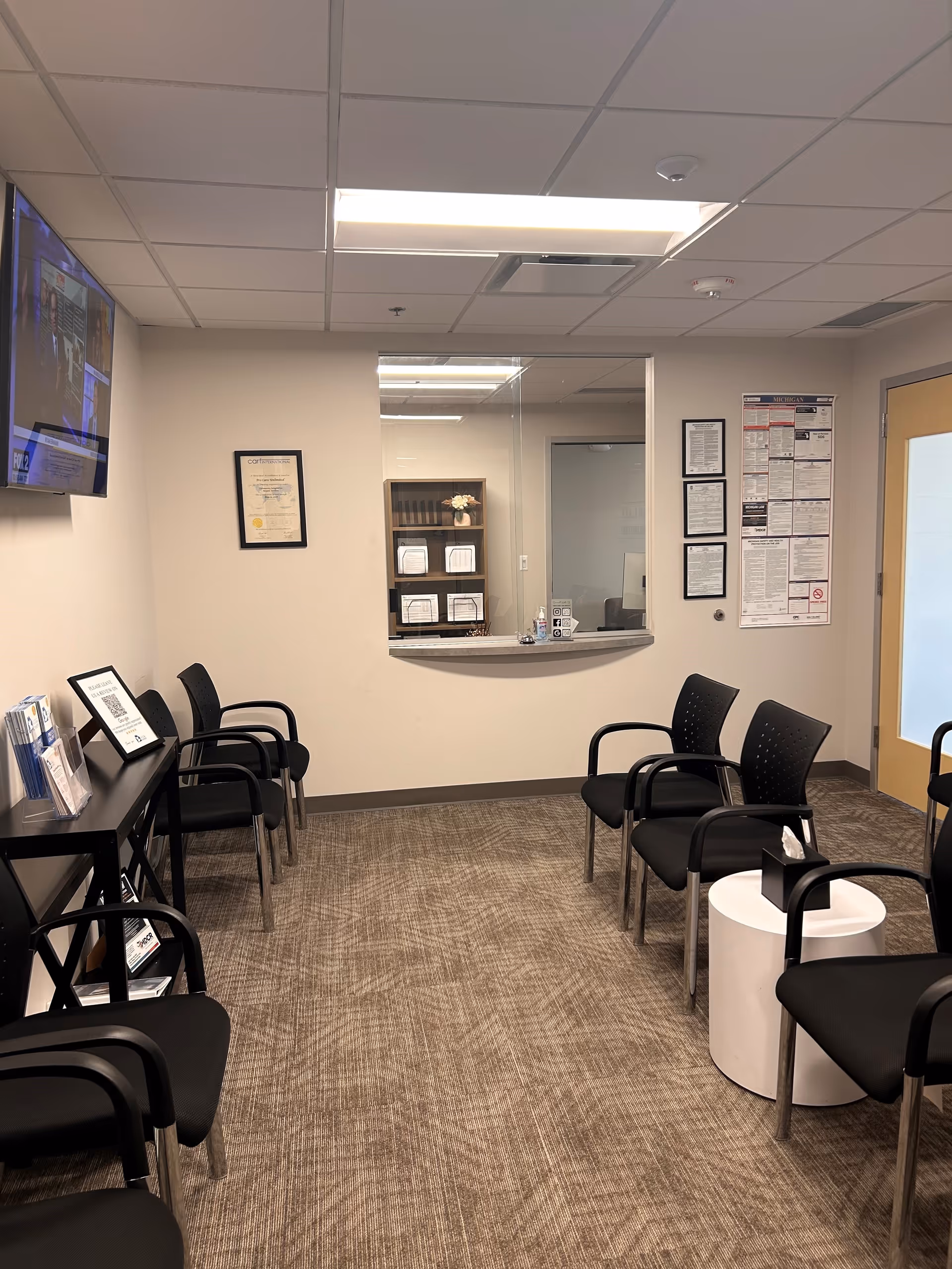 A reception lobby with black chairs, a front desk window, and wall posters.