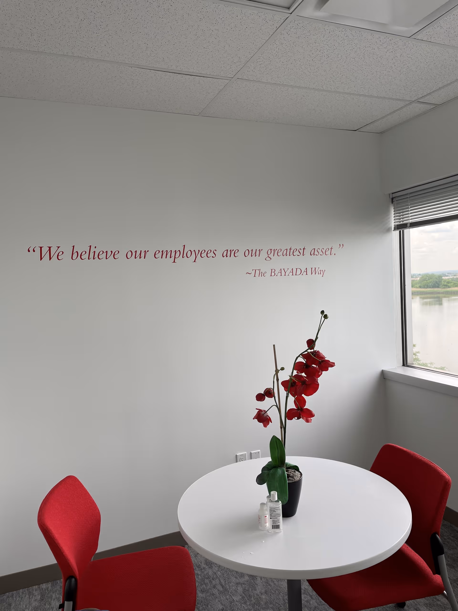 Interior corner with round white table, red chairs, wall quote, and a window view.