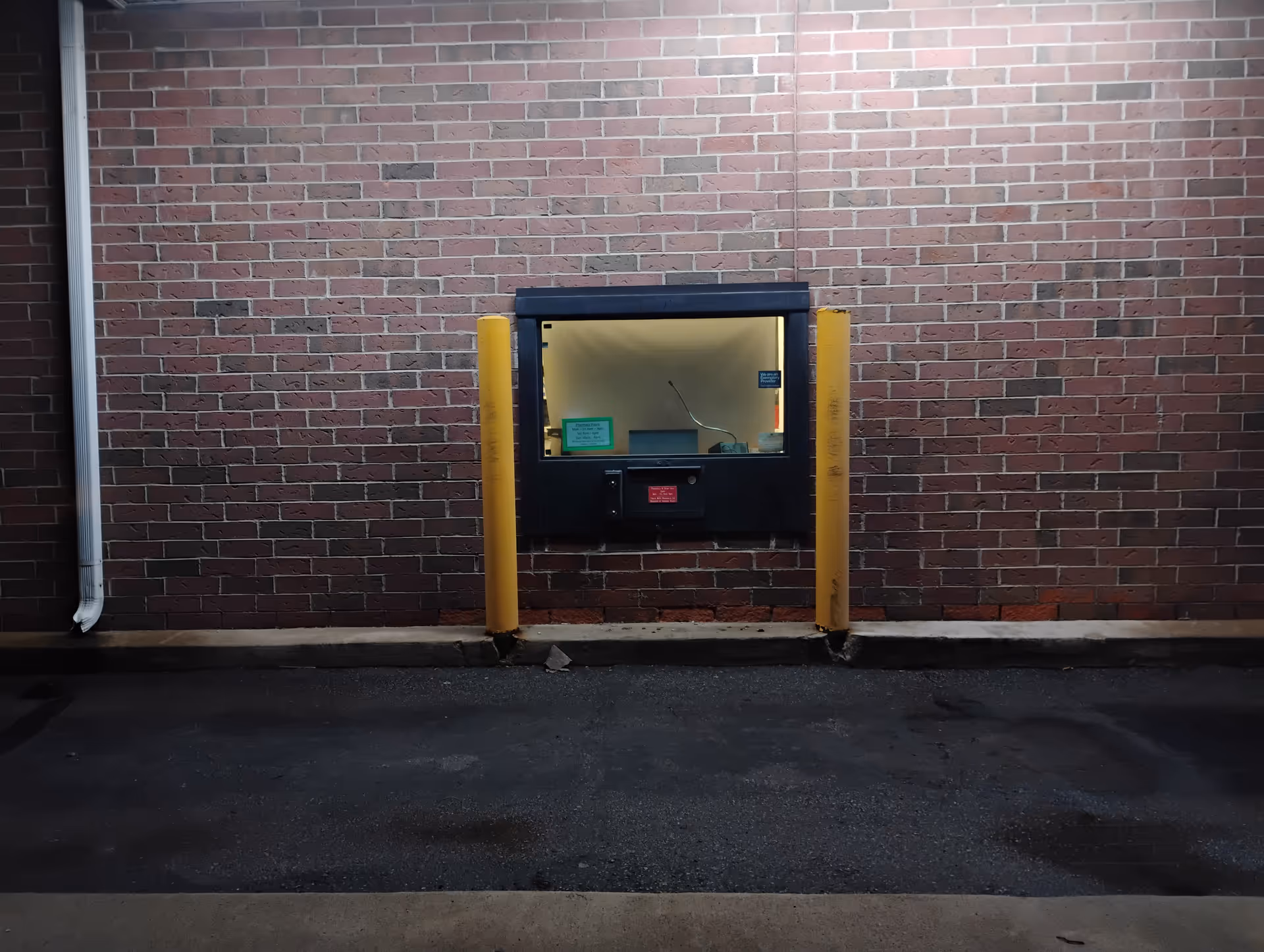 Exterior brick wall with a small service window and yellow protective posts.