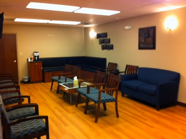 Cozy indoor senior living lounge with blue sofas, wooden chairs, and a coffee table.