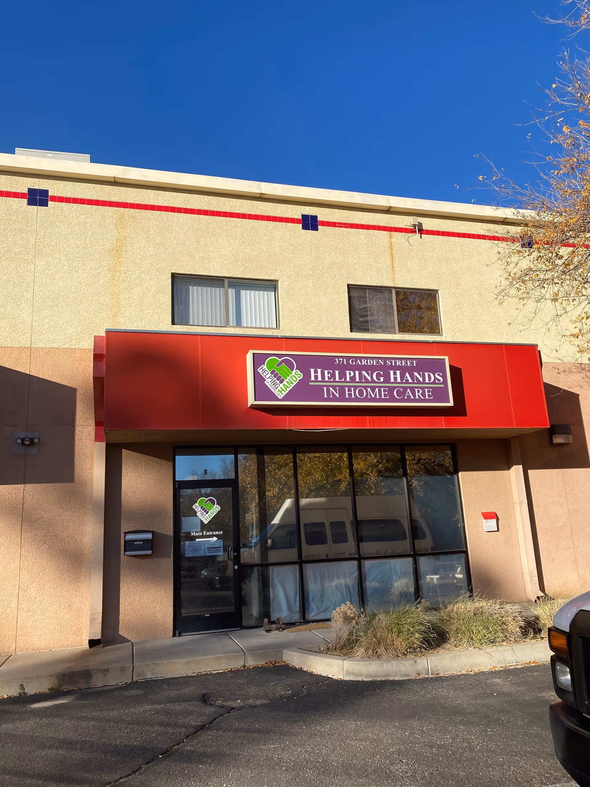 Front view of Helping Hands in Home Care building with red sign and glass doors.