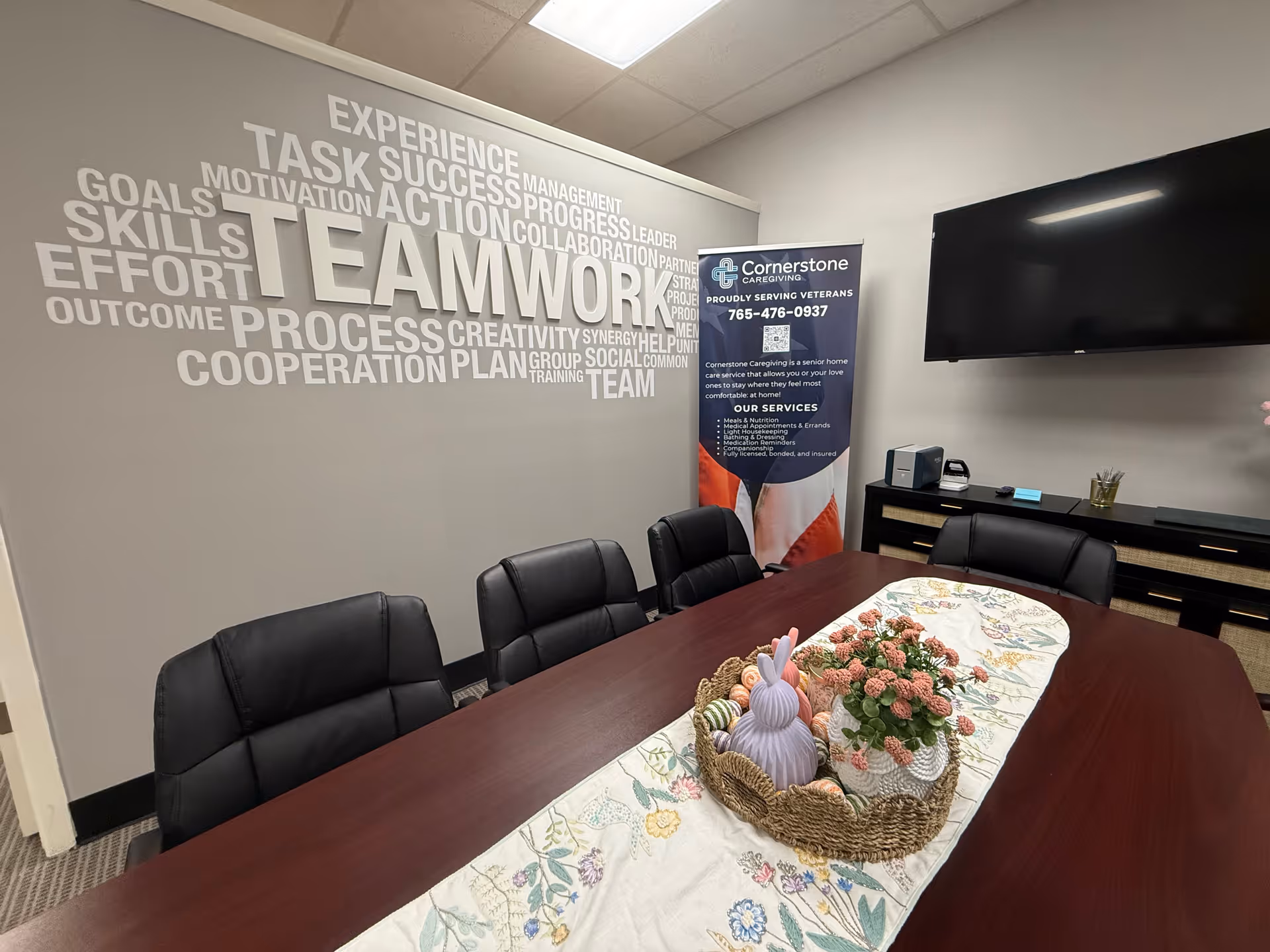 Interior conference room with a long table, black chairs, wall mural, and a Cornerstone banner.