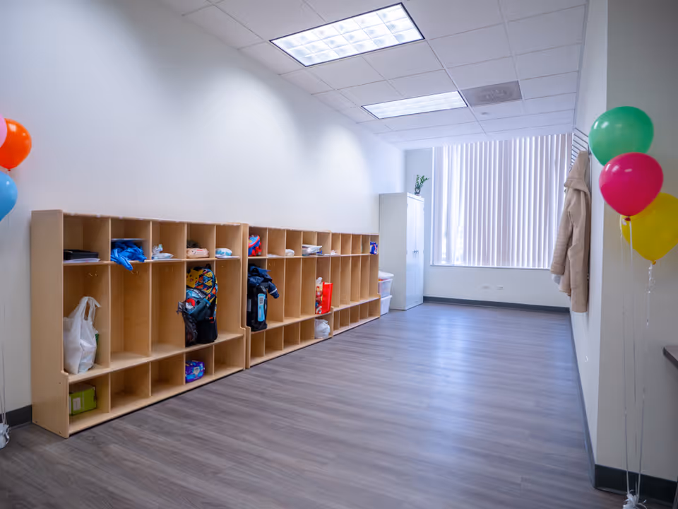 A spacious interior hallway with rows of cubbies, coats, bags, and balloons near the end.