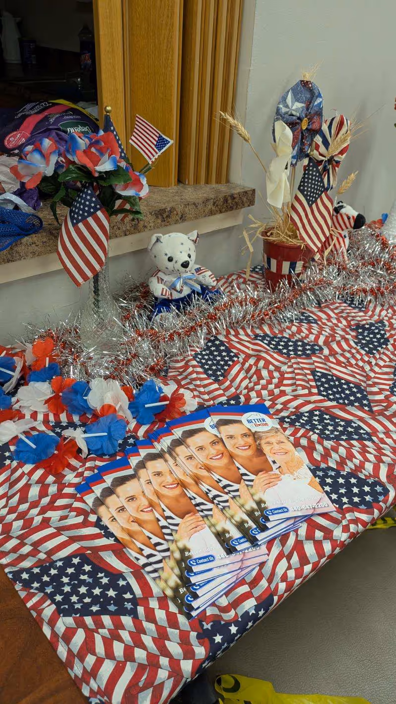 Patriotic table display with American flags, tinsel, flowers, and brochures featuring smiling faces indoors.
