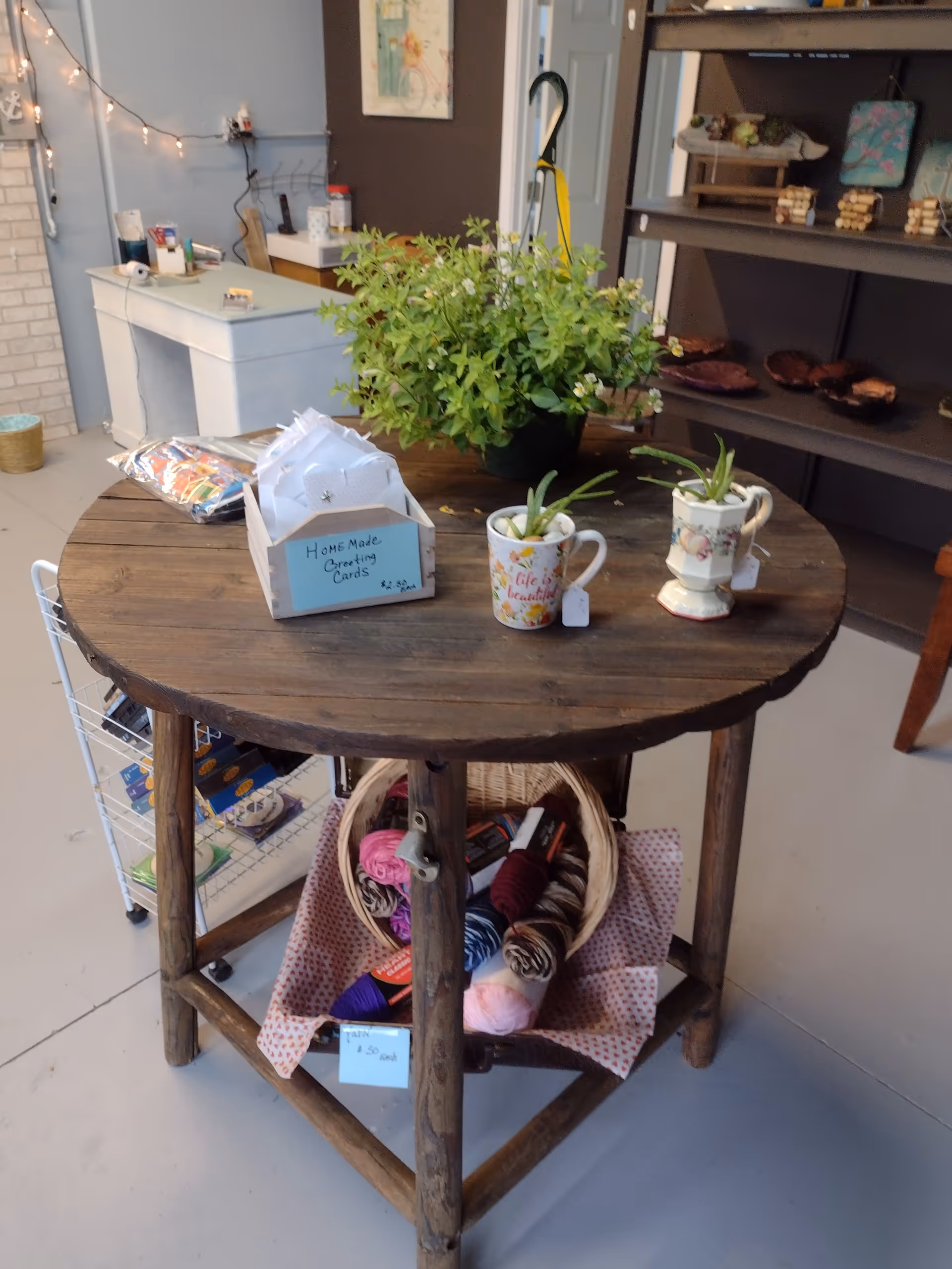 Round wooden table with plants, yarn, and craft supplies in a cozy indoor room