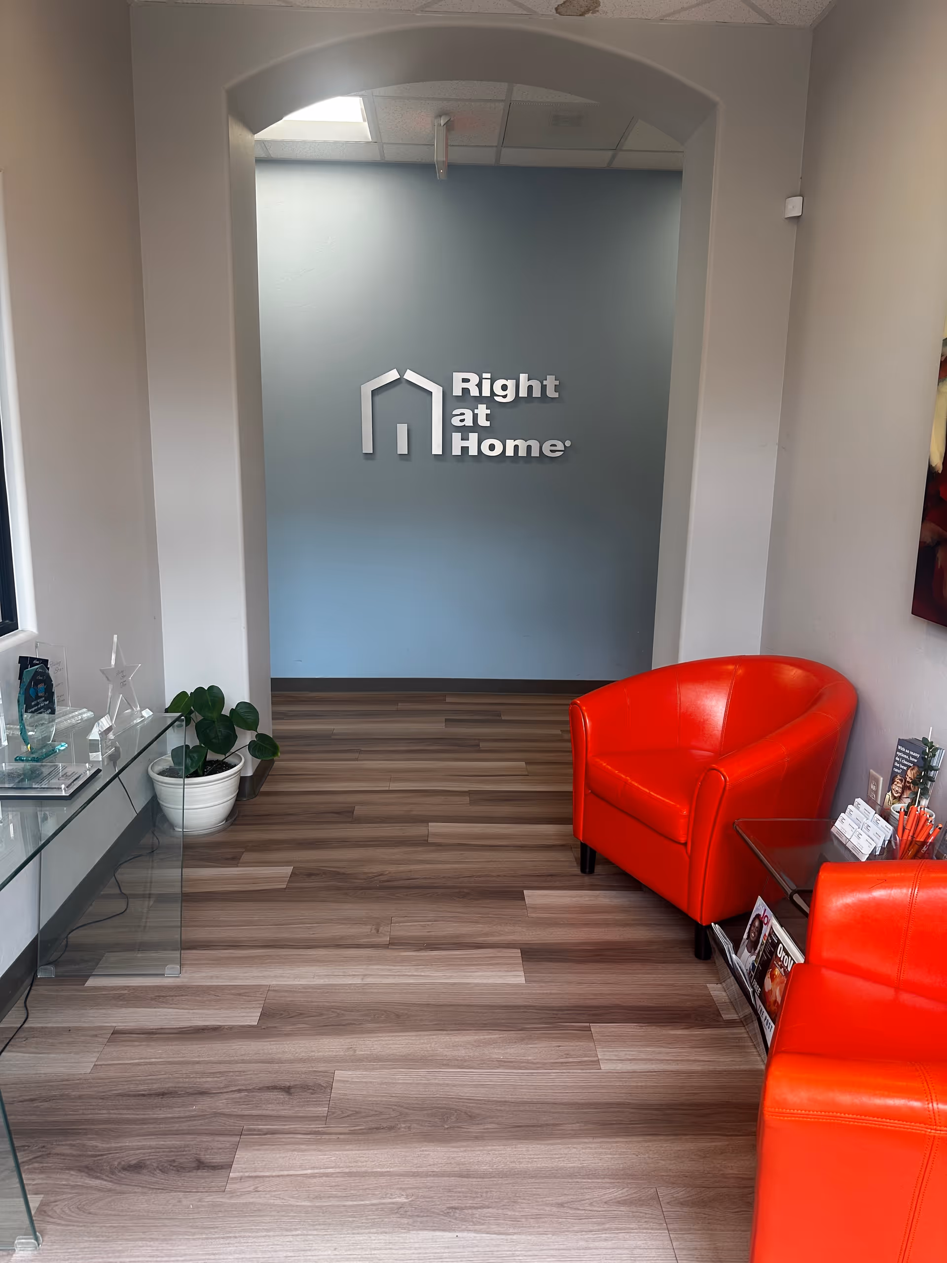 Interior reception area of Right at Home with blue wall, logo, glass table, and red chairs.