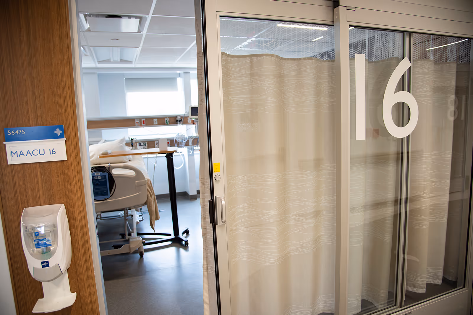 Hospital patient room interior visible through glass doors, bed and medical equipment.