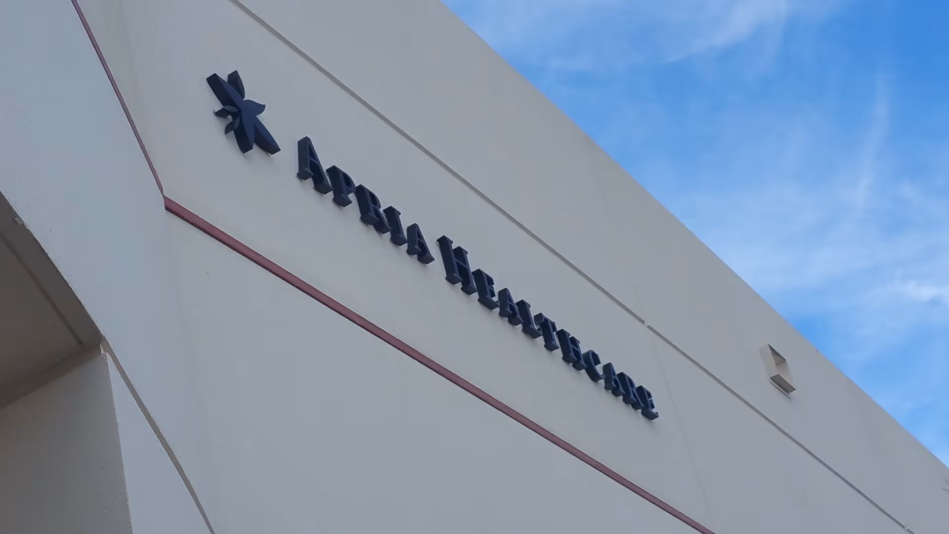 Exterior view of a white building with Apria Healthcare sign under blue sky.