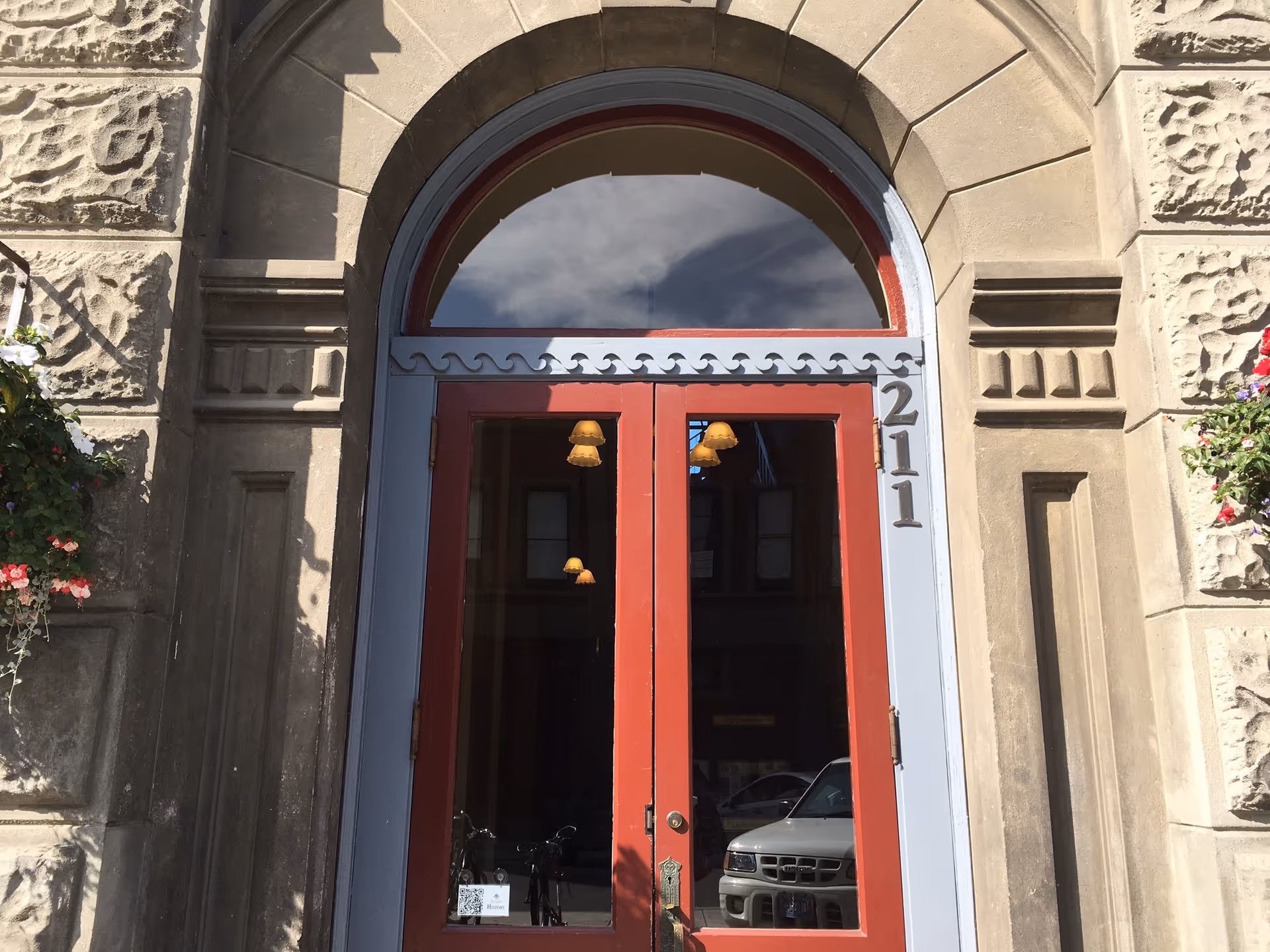 Stone building entrance with red double doors and arched window above.