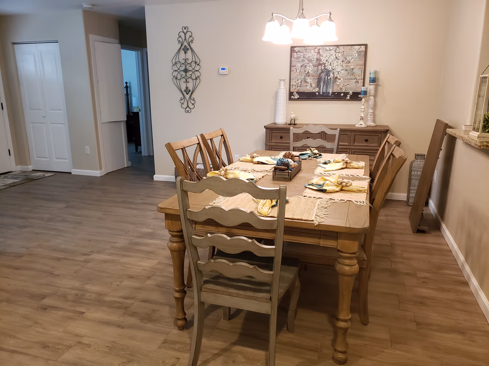 A wooden dining table with six chairs set with placemats in a well-lit dining room.