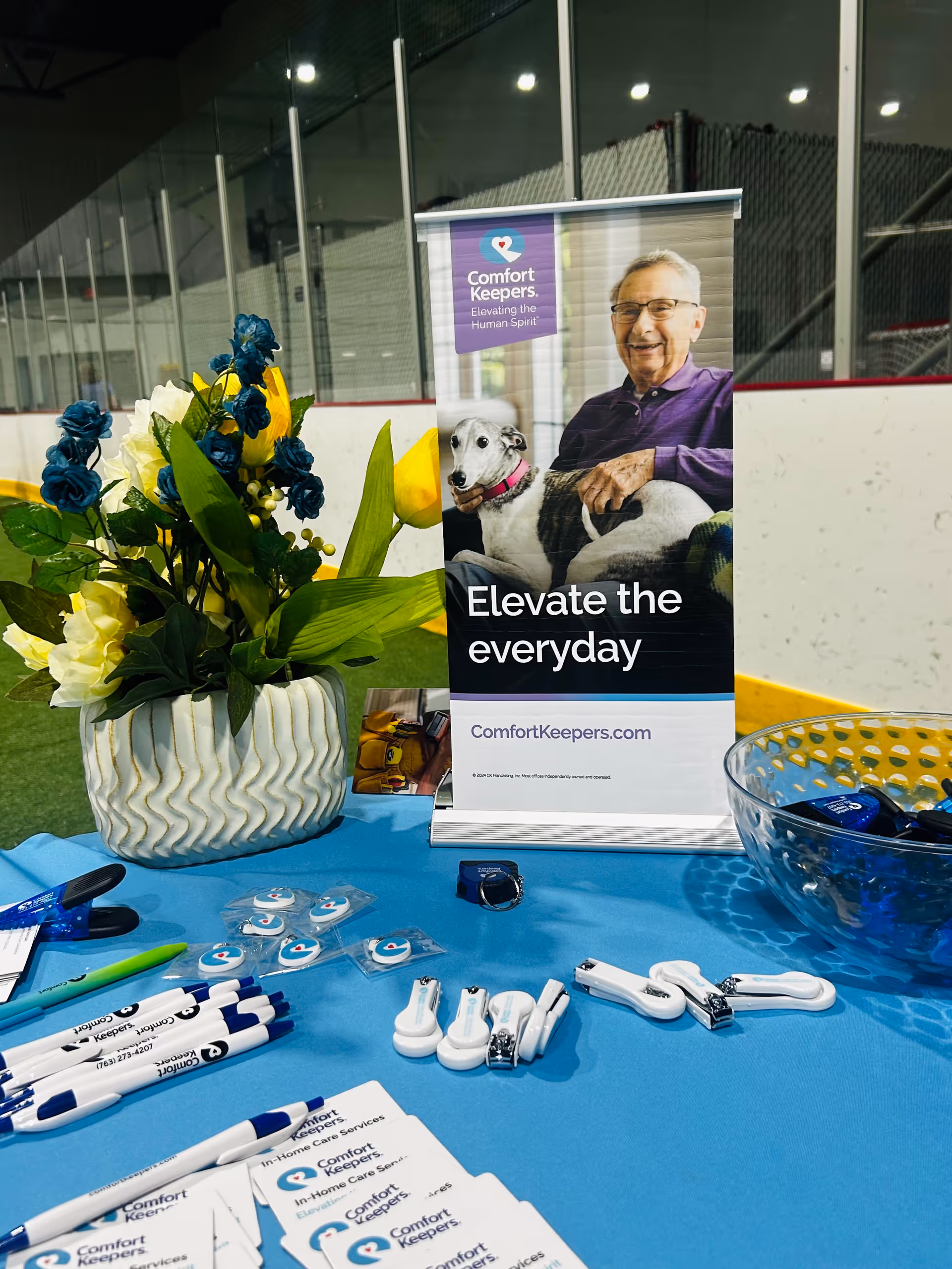 Promotional Comfort Keepers display with a banner, flowers, and brochures on a blue table.