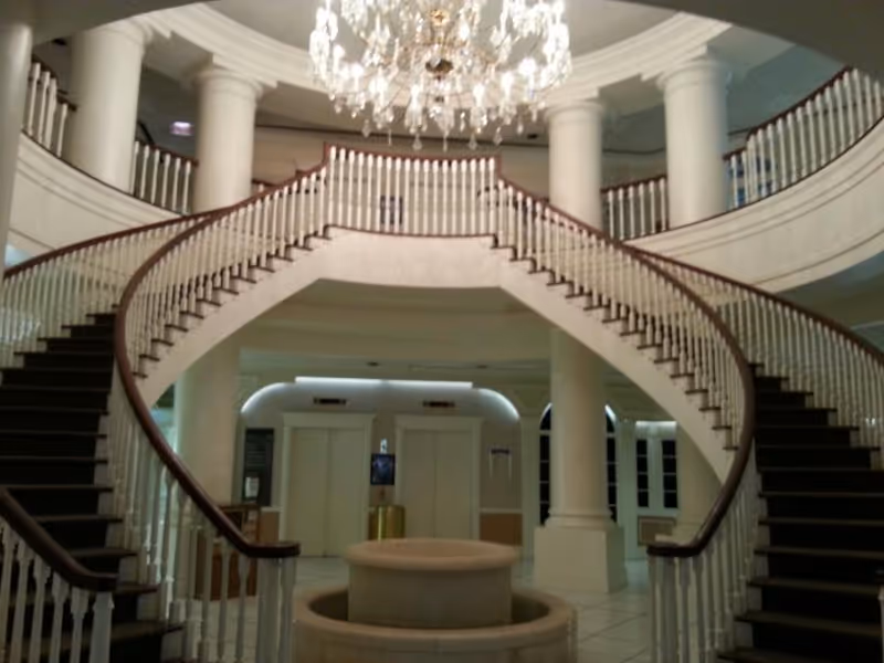 Canon Hospice lobby features a grand curved staircase, chandelier, and white columns.