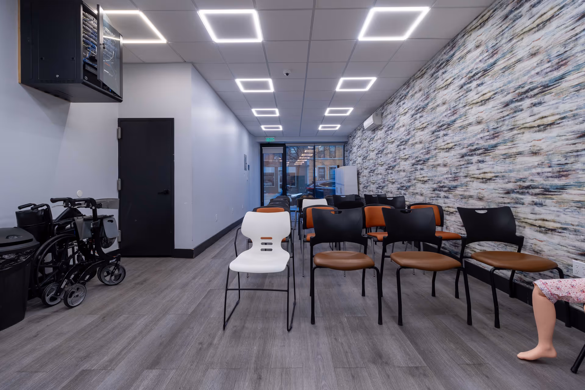 A modern indoor waiting area with chairs, a wall mural, and wheelchairs along the left.