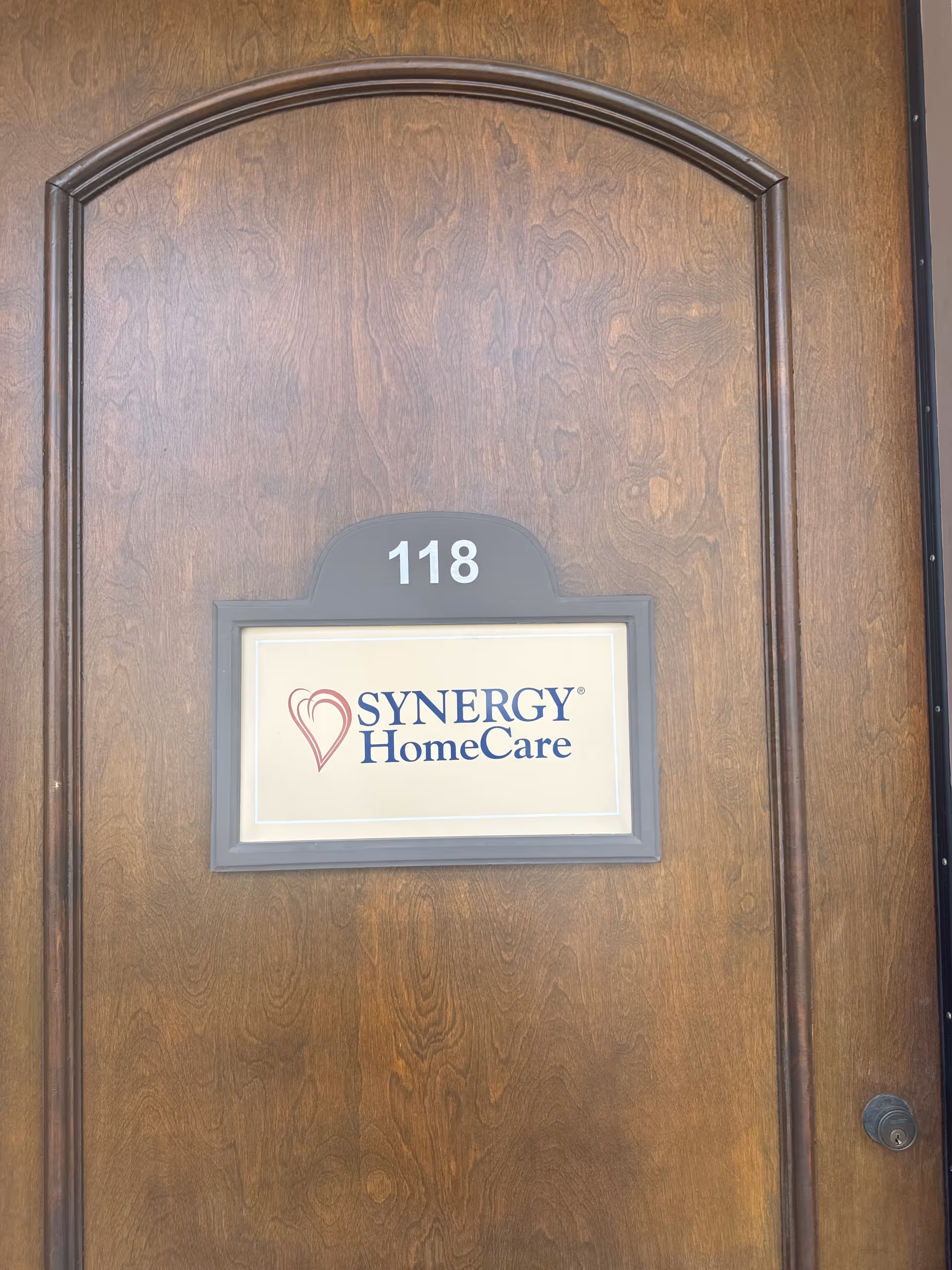 A wooden door with number 118 and a Synergy HomeCare sign mounted on a dark frame.