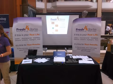 Exhibition booth for Fresh Starts Behavioral Therapy with banners, table, brochures, and a projection screen.