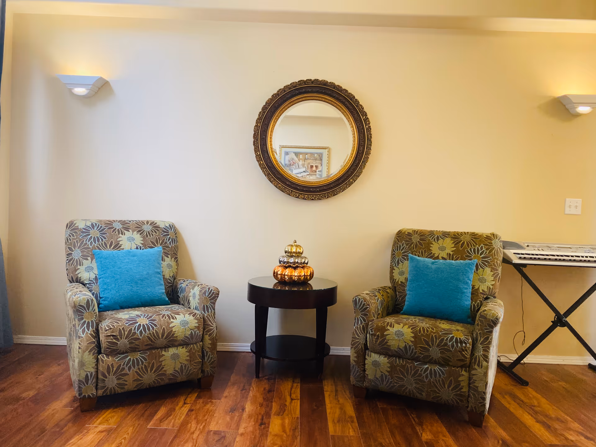 Cozy seating area with two patterned armchairs, teal pillows, and a round wall mirror.