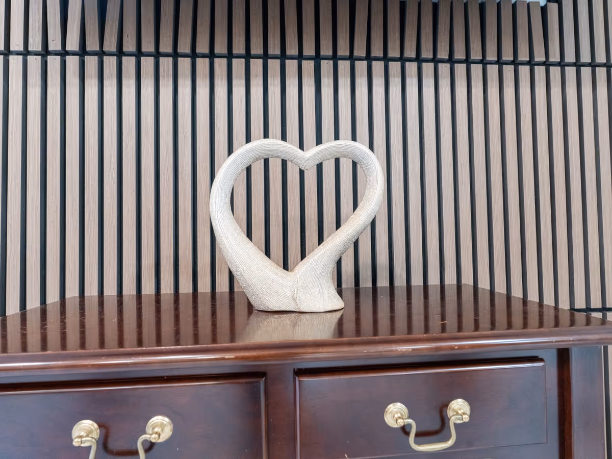 A wooden dresser with a heart-shaped sculpture on top against striped wall.