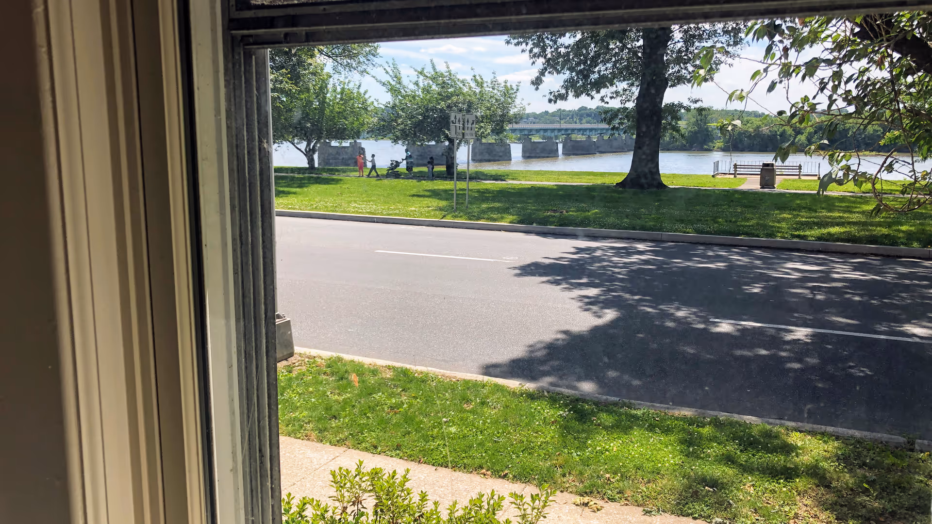 View from inside a building toward a riverfront park with pedestrians.