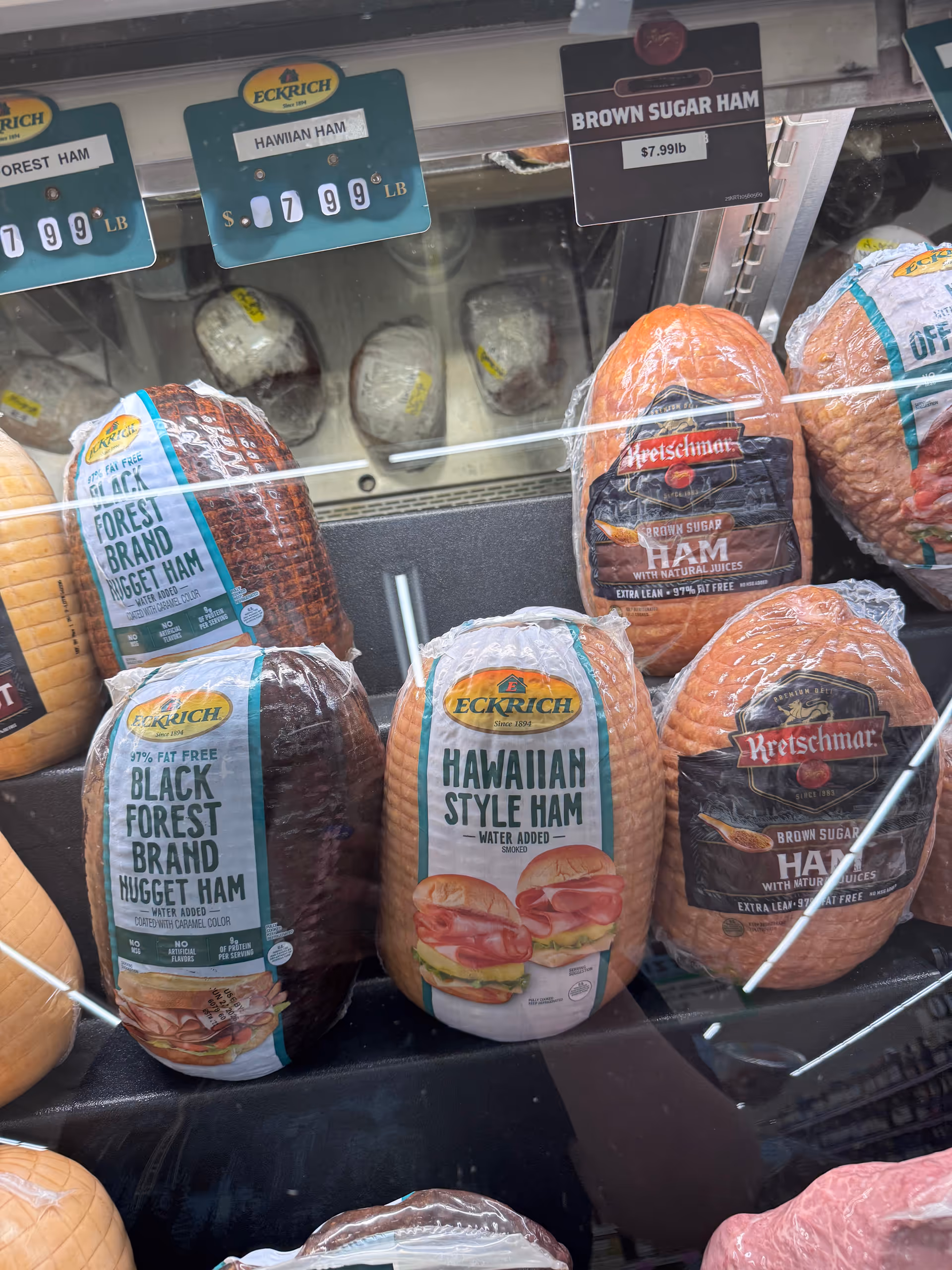Assorted deli hams displayed in a glass refrigerated case at Discount Drug Mart.