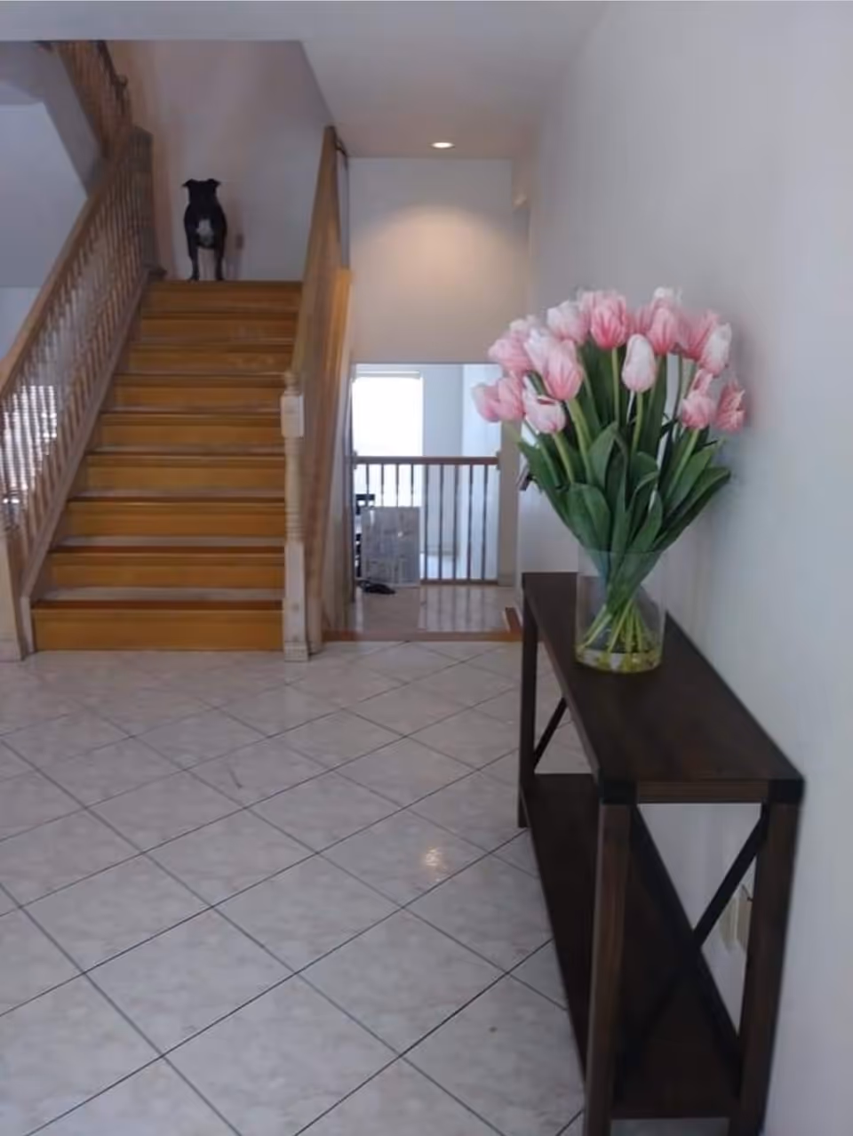 Interior foyer with wooden staircase, railing, and a vase of pink tulips on a console table.