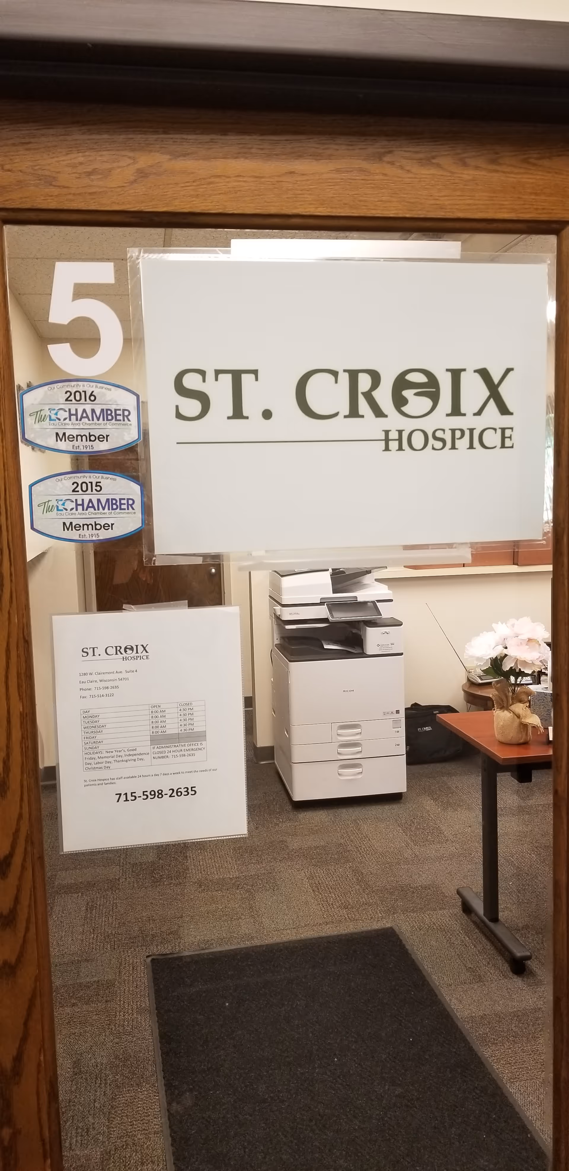 Interior doorway shows St. Croix Hospice sign with office printers and furniture.