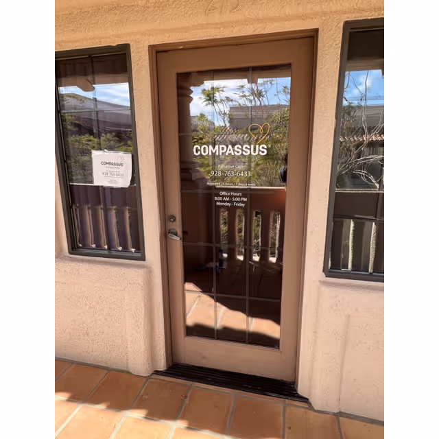 Entrance door with Compassus logo, hours, and windows on tan exterior wall.