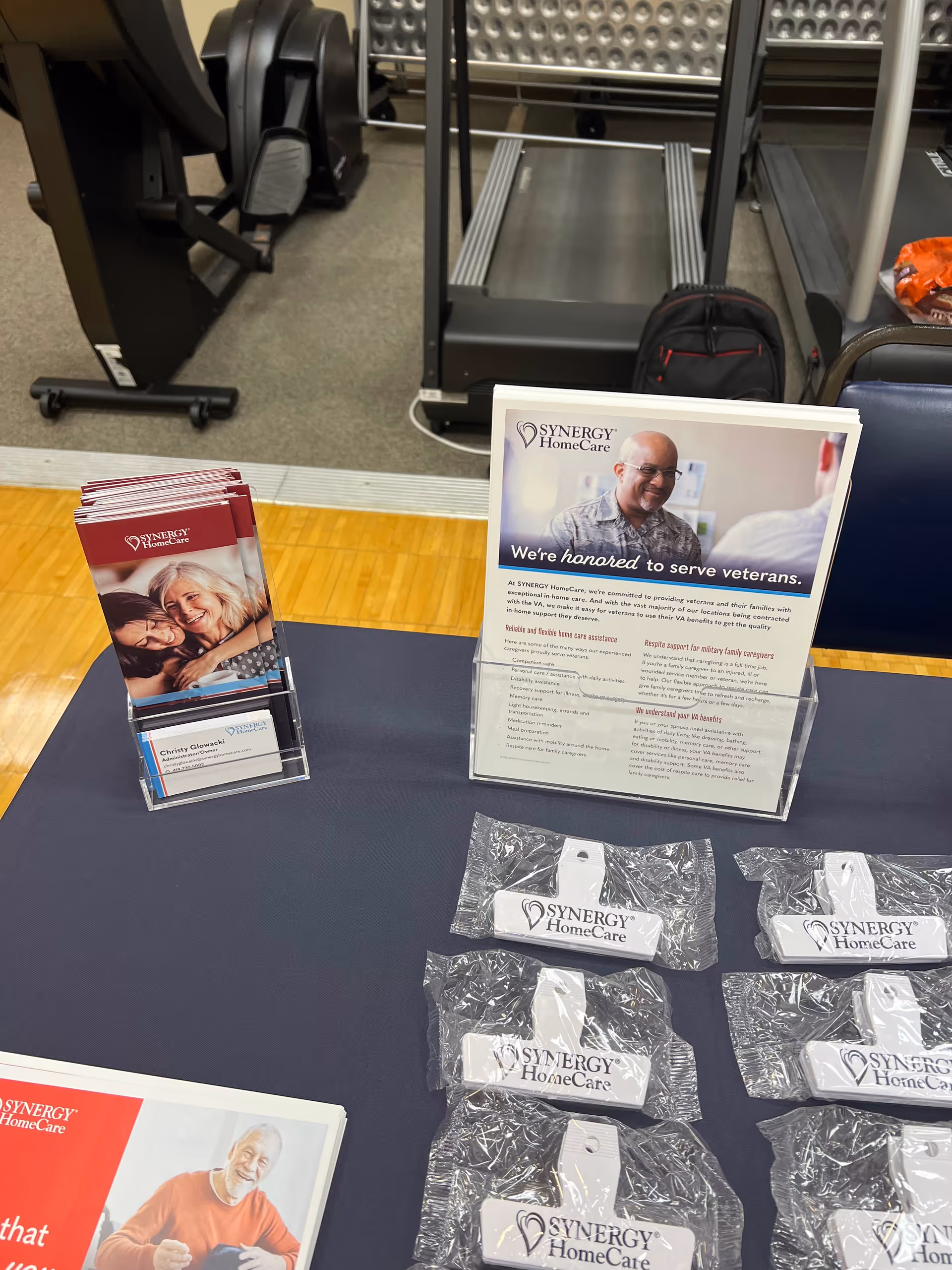 Table with Synergy HomeCare brochures and branded items in a gym-like interior.
