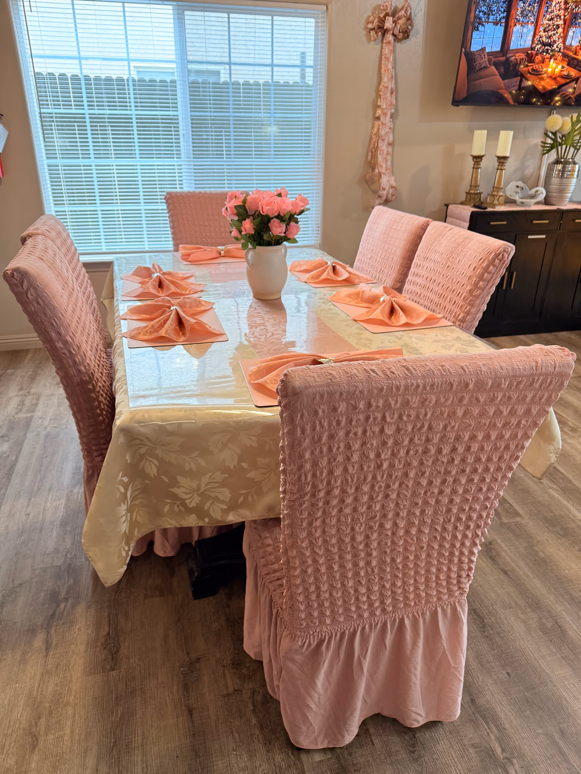 Pink-draped dining table with folded napkins, vase of pink flowers, and matching chairs.