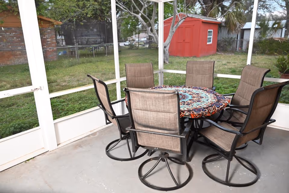 Outdoor screened patio with a round table and six cushioned chairs.