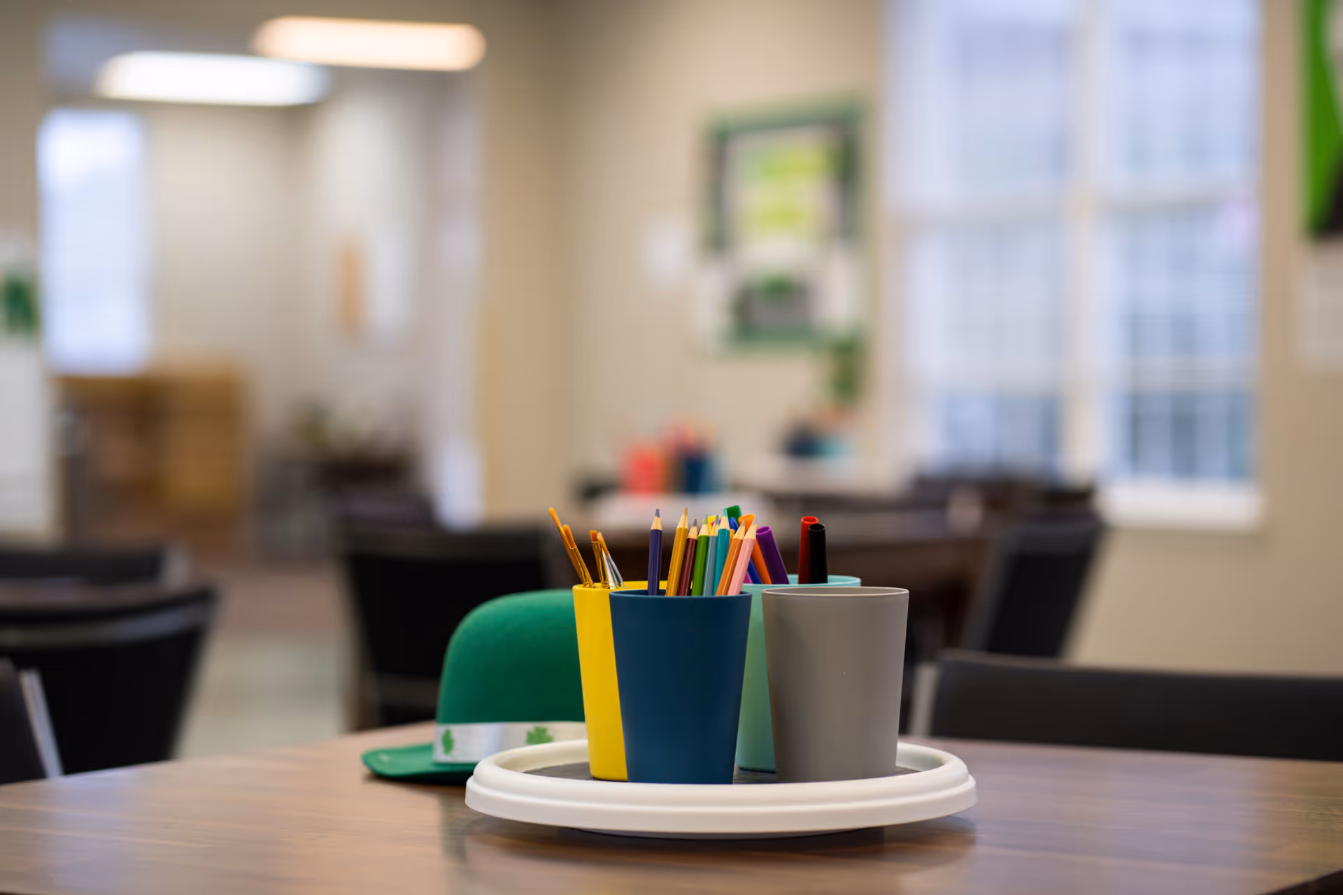 Colorful pencils in cups on a wooden table in a bright activity room.