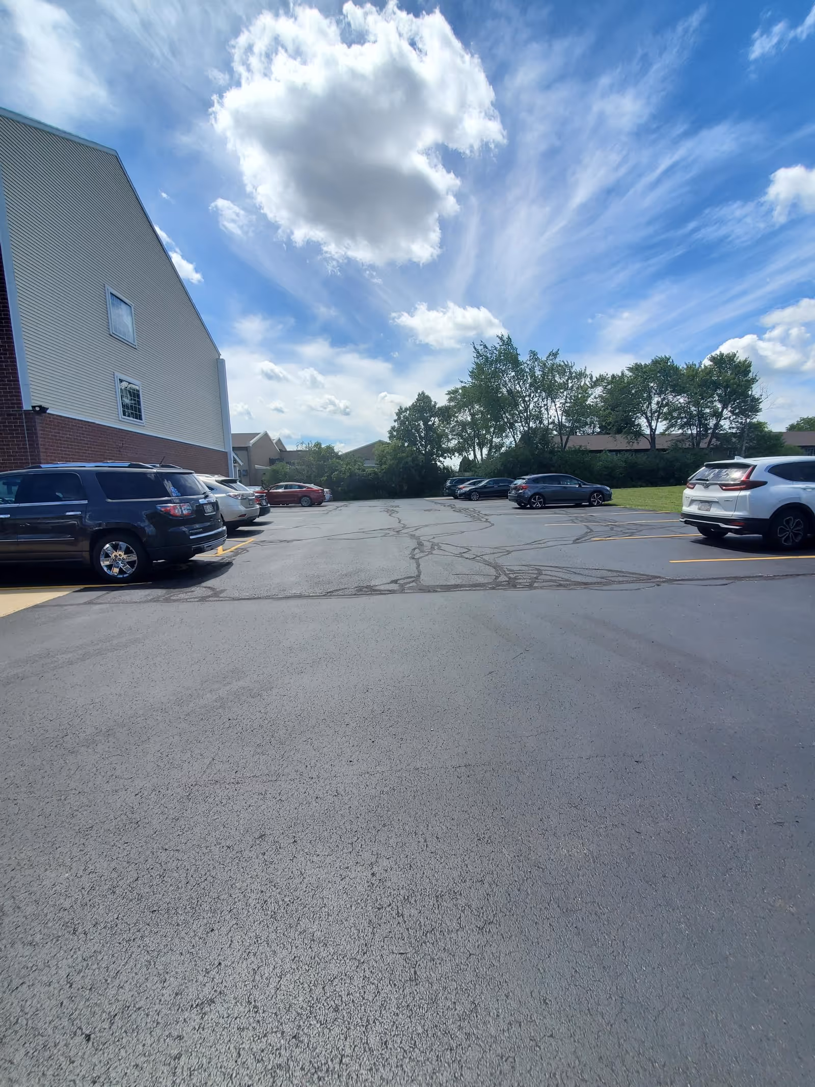 Exterior view of a senior living campus with parked cars and blue sky.