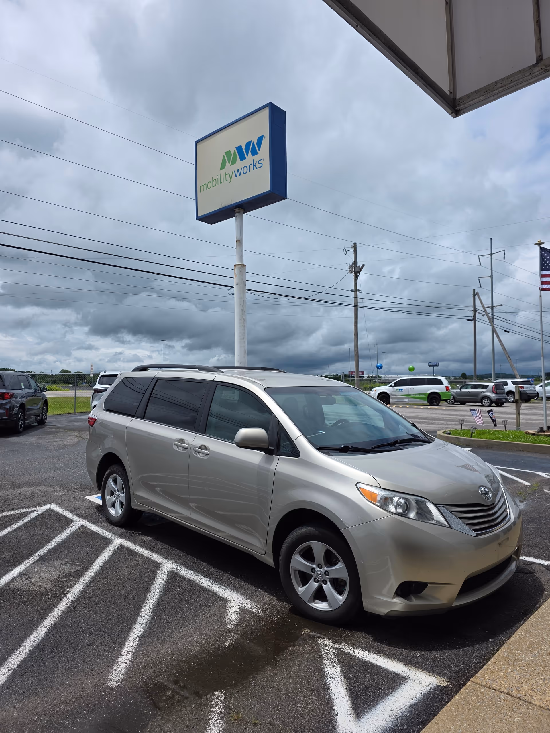 Silver minivan parked in a lot beneath a MobilityWorks sign.