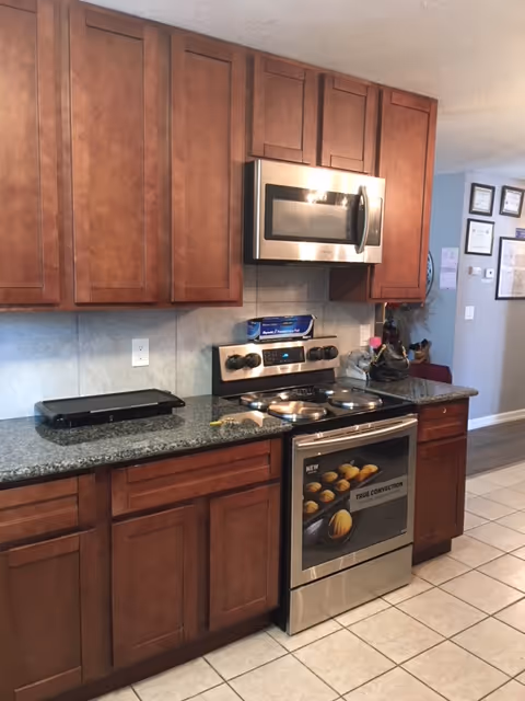 Modern kitchen with wooden cabinets, stove, microwave, and granite countertops.