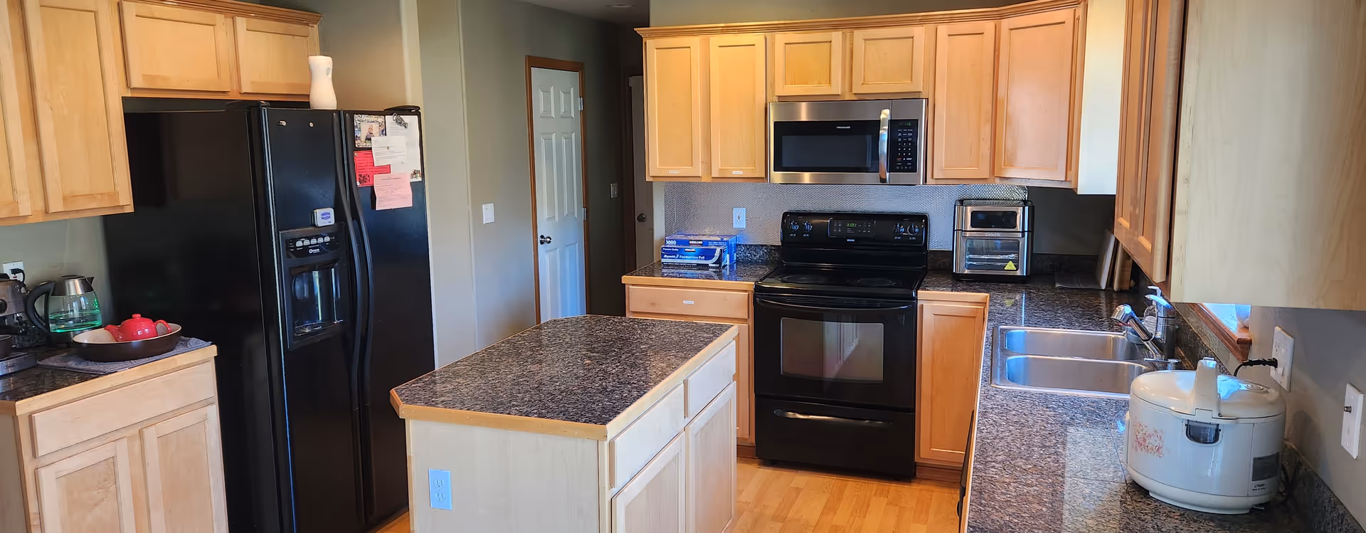 Bright kitchen with granite countertops, wooden cabinets, stainless appliances, and an island.