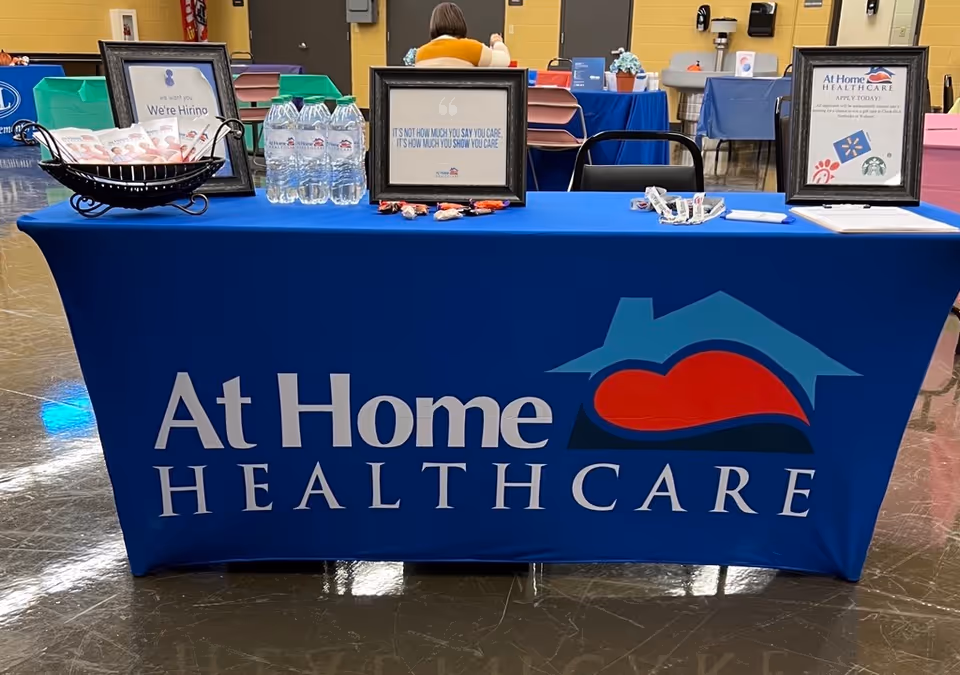 Blue table with At Home Healthcare logo, water bottles, and framed informational signs.