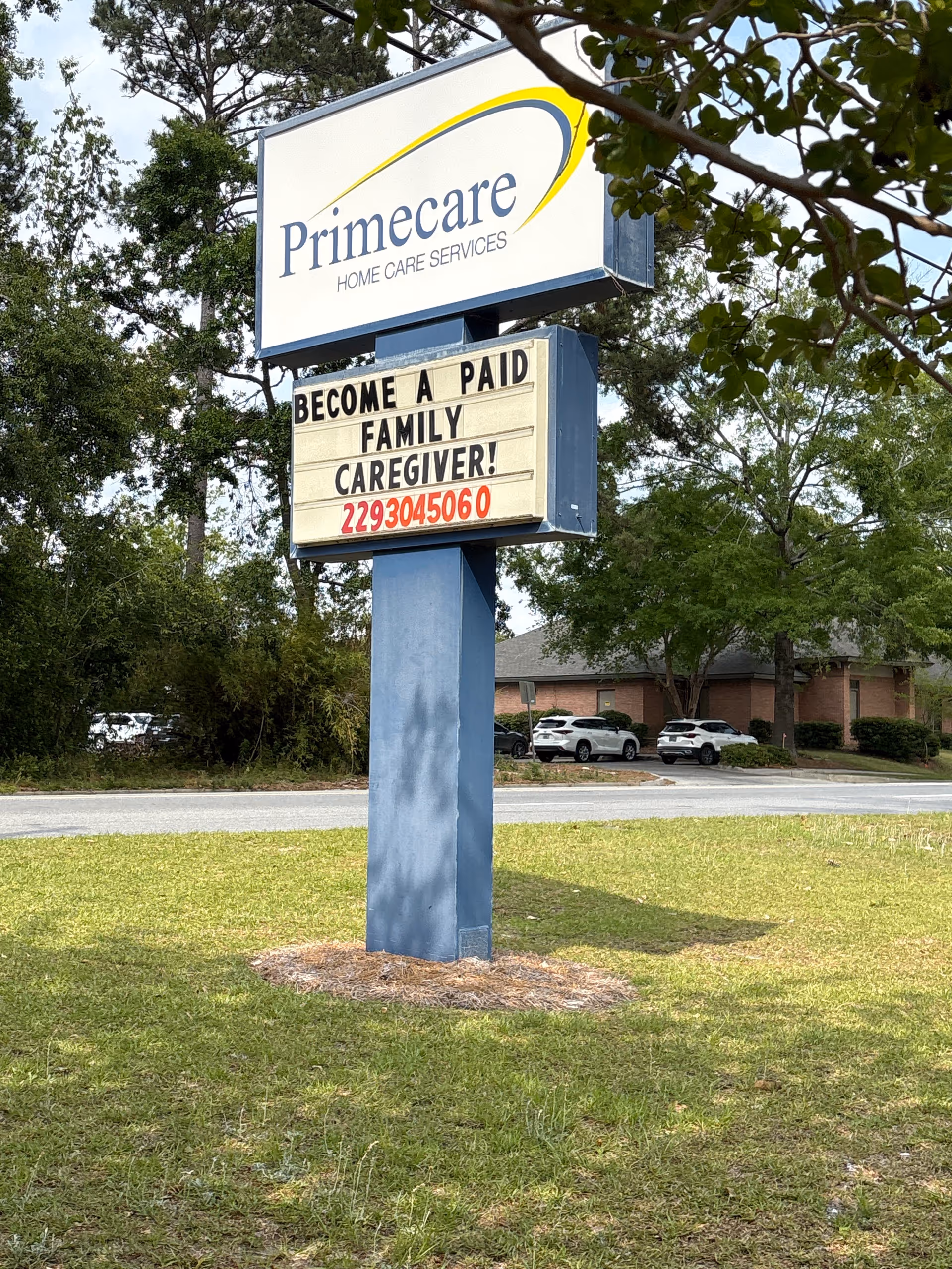 Outdoor sign reading Primecare Home Care Services stands on a grassy lot near a brick building.