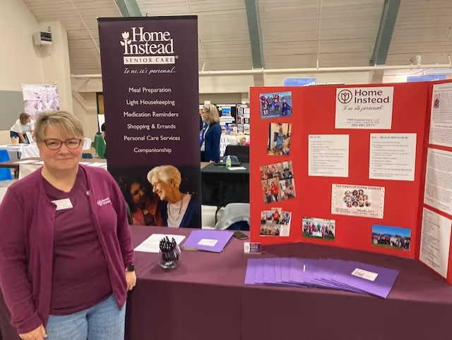 Indoor Home Instead booth with banners, a table, and a staff member present.