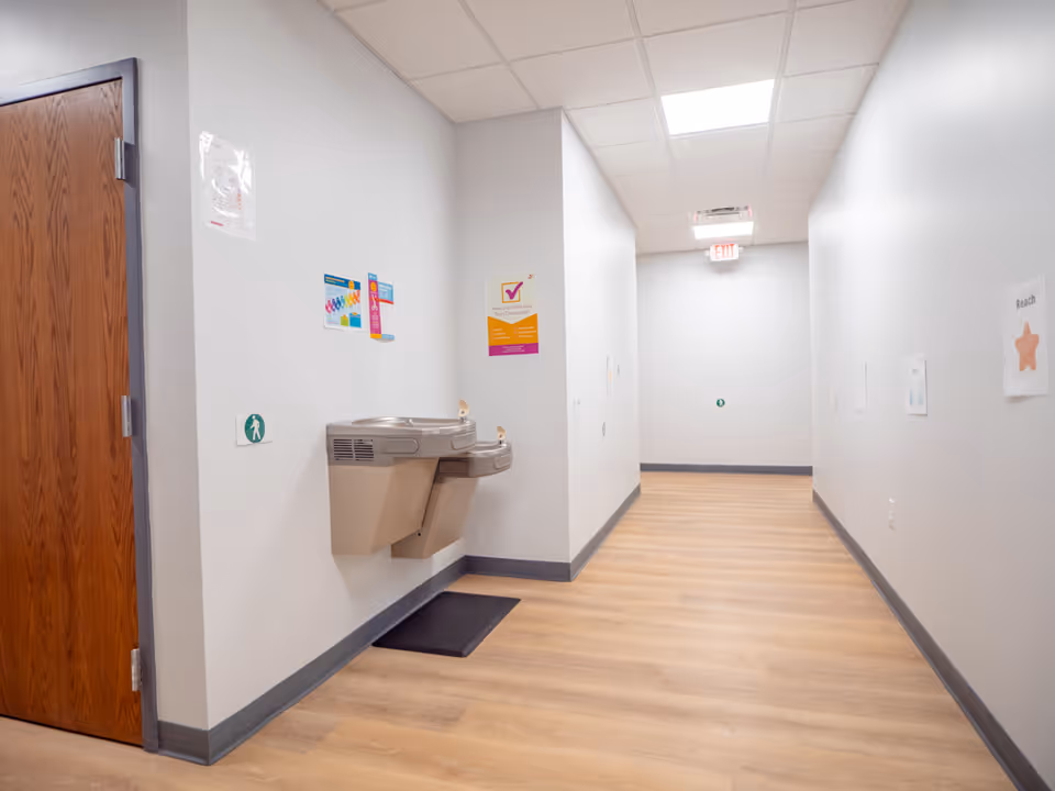 Narrow hallway with a wall-mounted drinking fountain and exit sign.