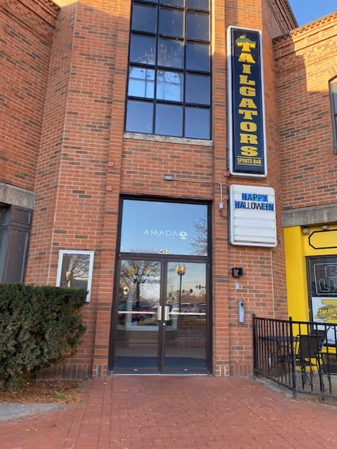 Brick building storefront showing Amada entrance and a Halloween sign.