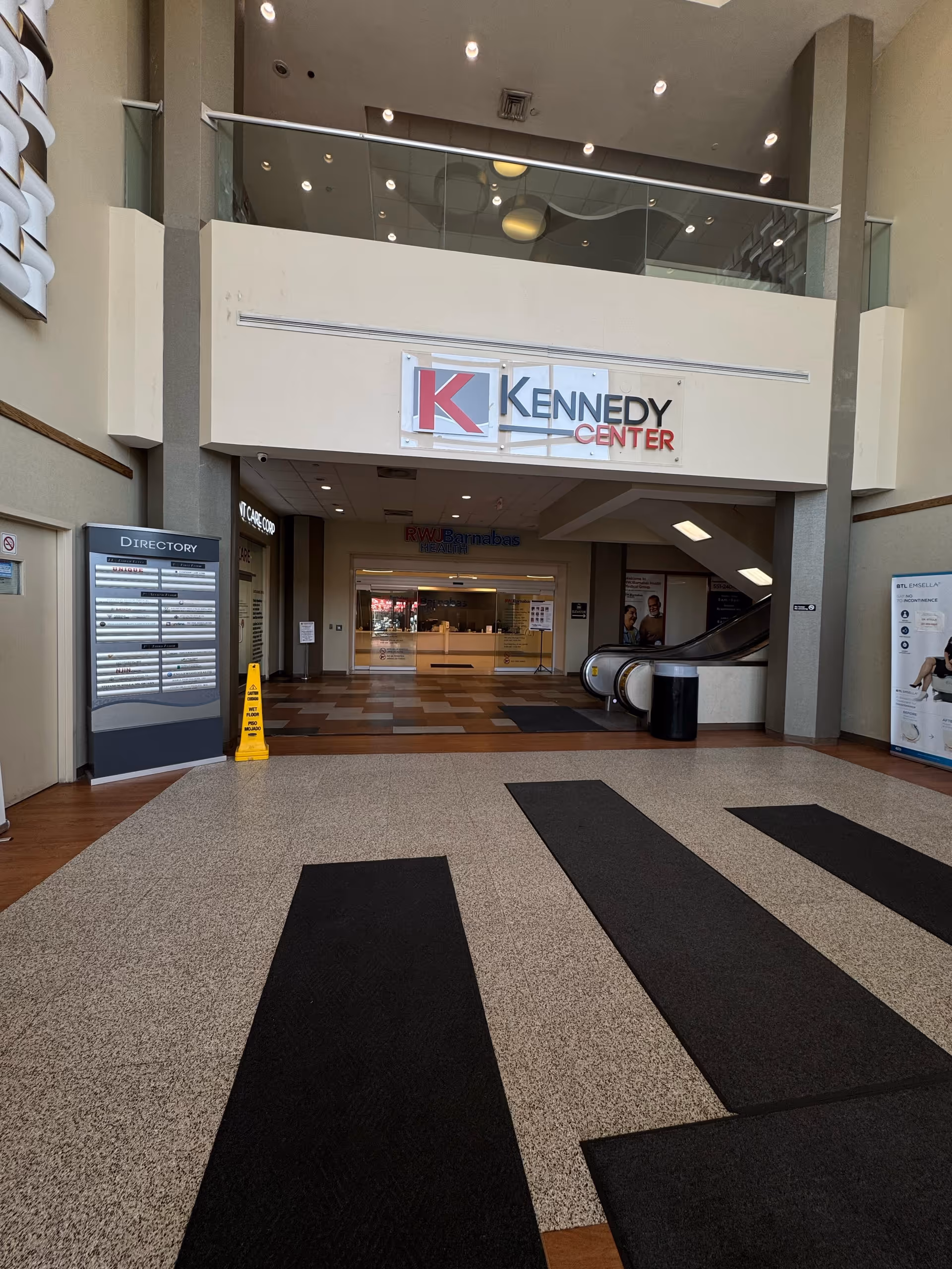 Interior mall-like lobby featuring Kennedy Center sign, escalators, directory board, and black patterned flooring.