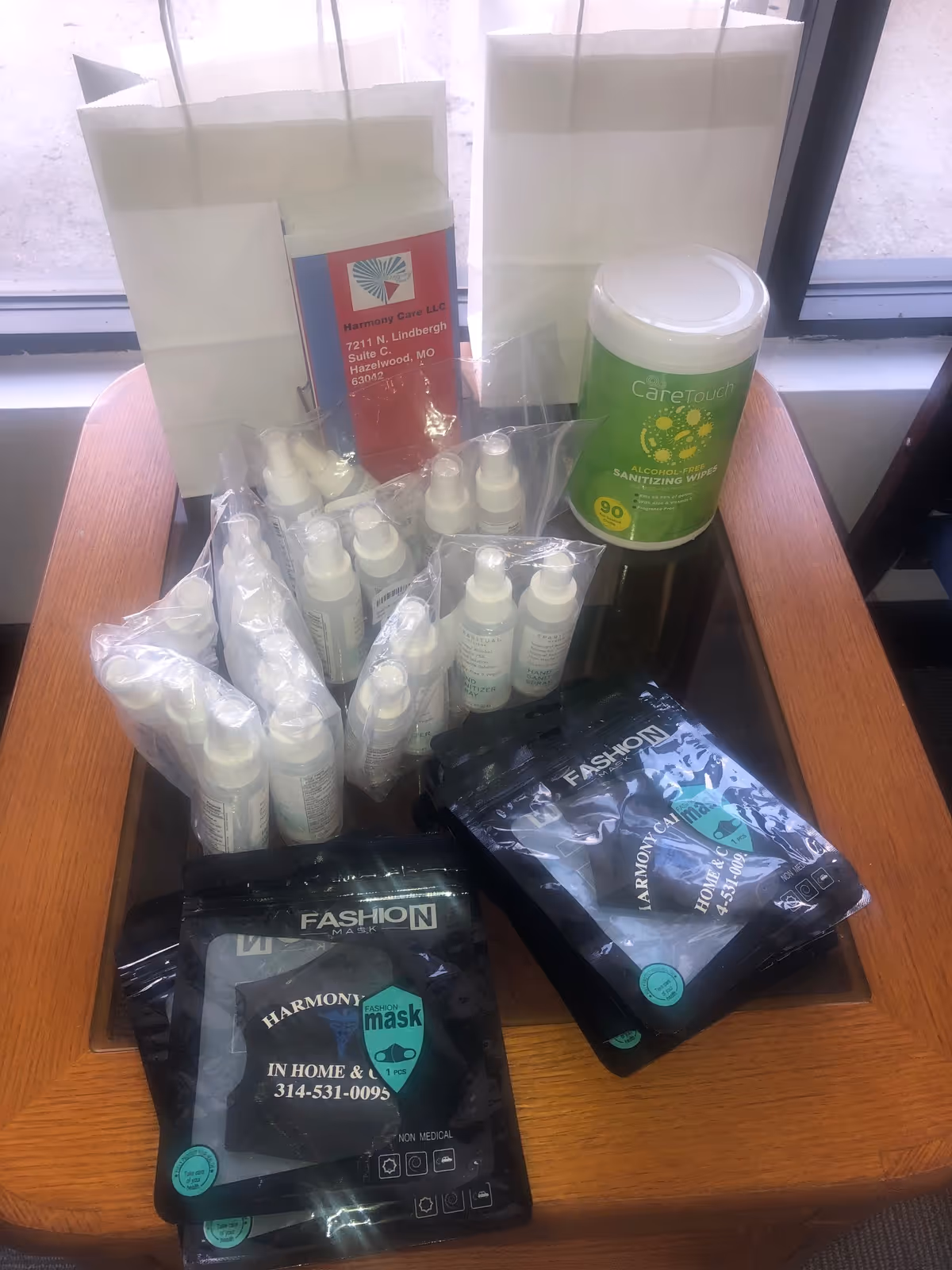 Table by window with Harmony Care supplies, sanitizer bottles, masks, and care products.