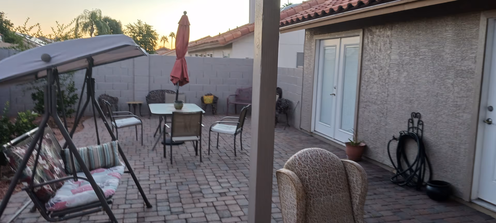 Outdoor patio area with table, chairs, swing, umbrella, and potted plants.