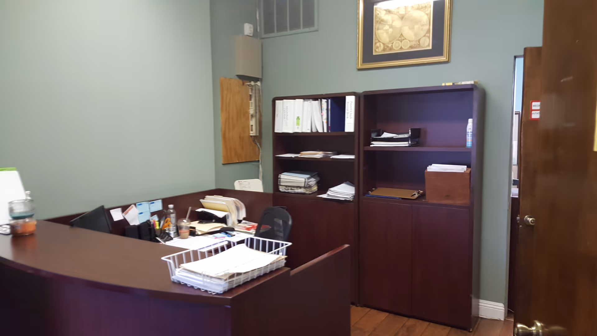 Office reception area with a curved desk, shelves, and clutter.