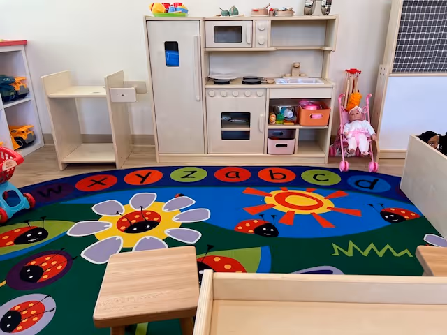 Colorful indoor play area featuring a wooden toy kitchen, stroller, and alphabet rug.