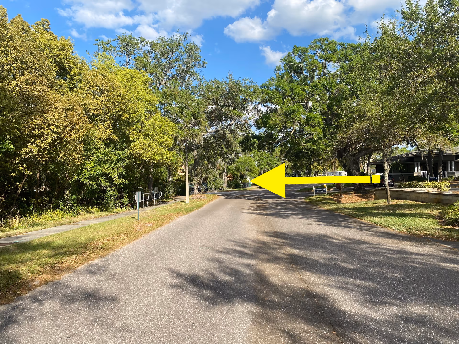 Tree-lined road leading to a building entrance on the right, with a large yellow arrow overlay.