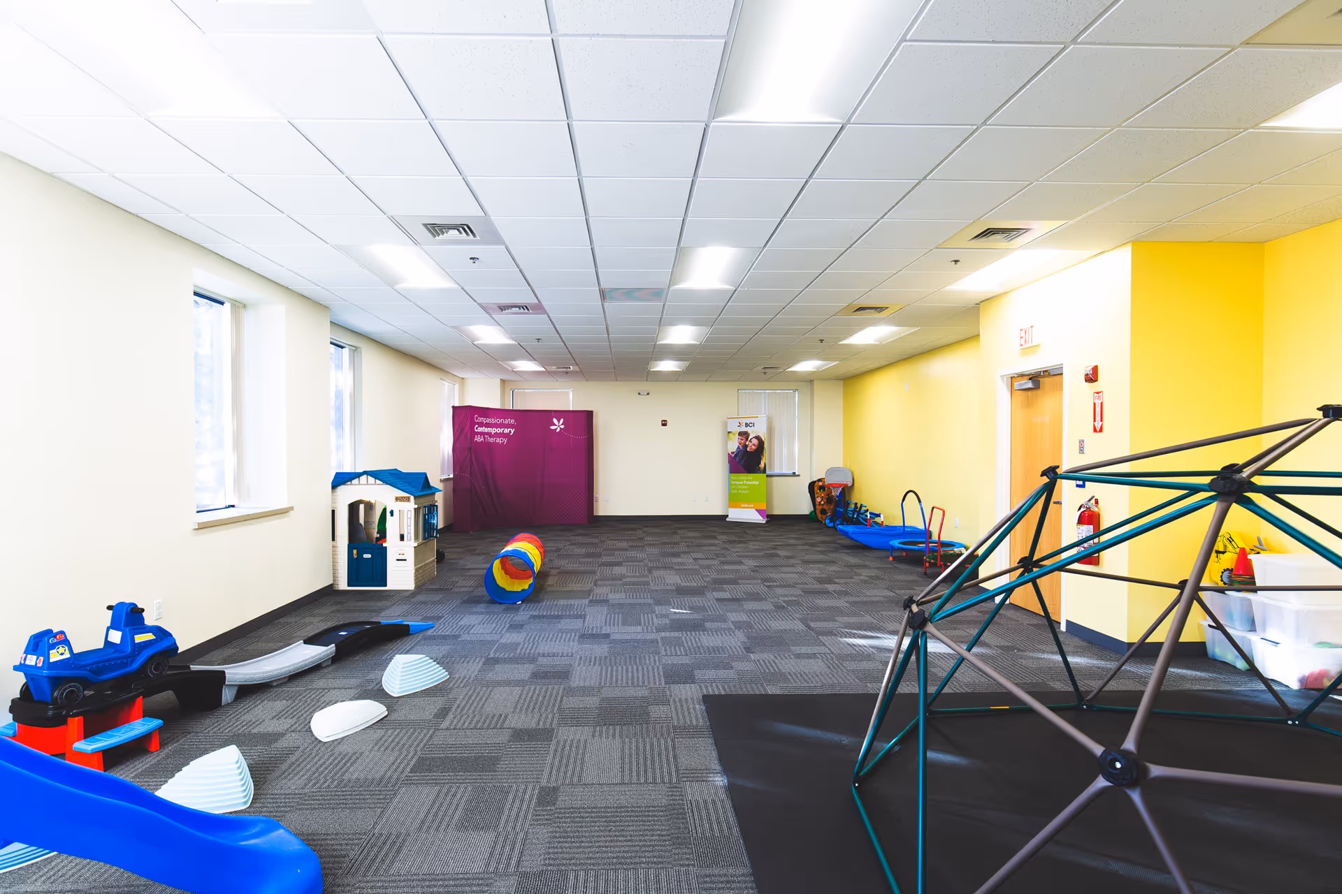 Bright indoor activity room with toys, a playhouse, and a climbing dome.