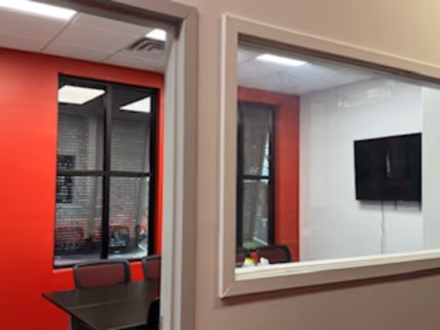 Interior view of a red-walled meeting room with a table, chairs, and a wall-mounted TV.