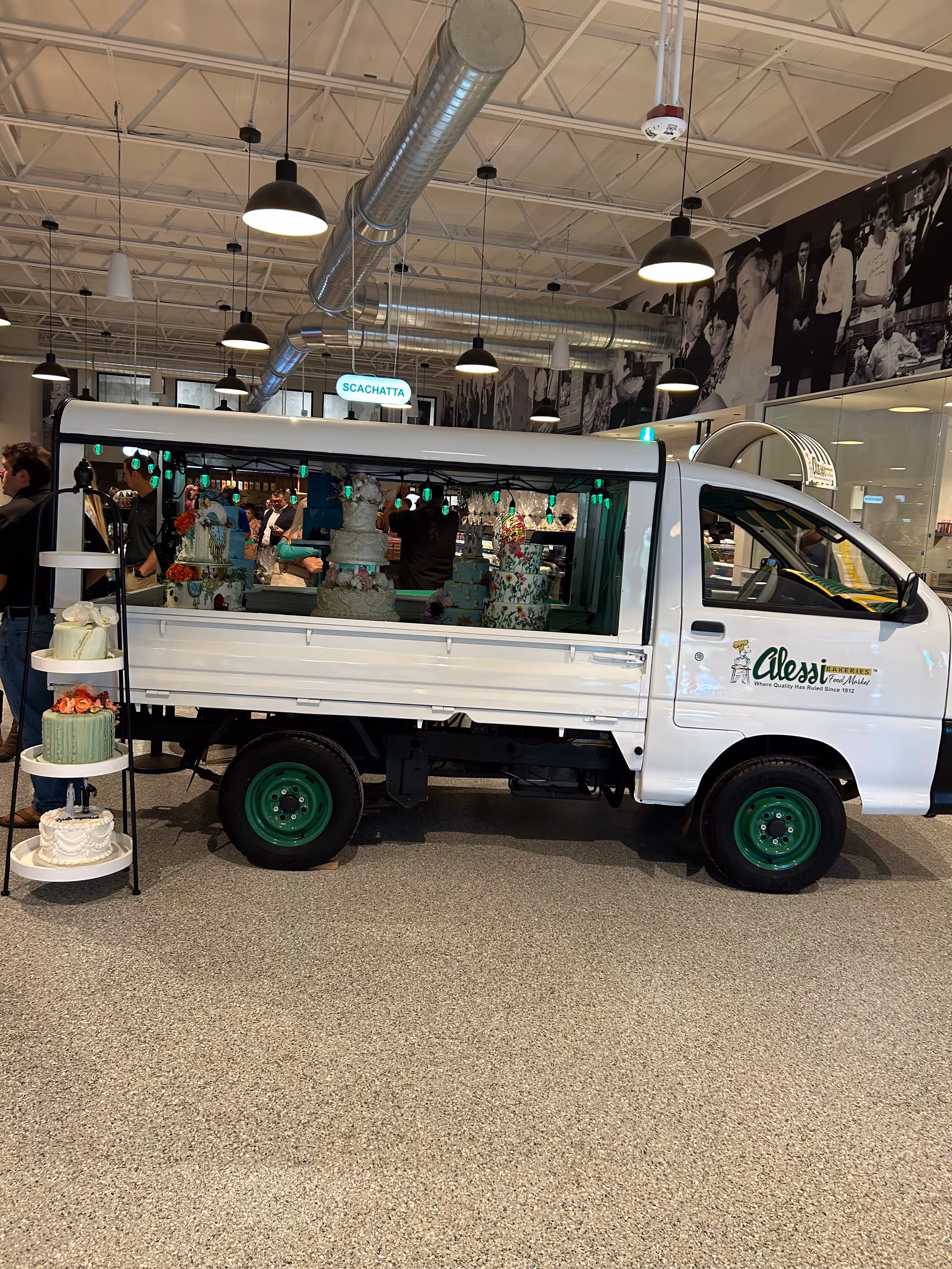 Inside a showroom, a white cake truck is displayed with tiered cakes.